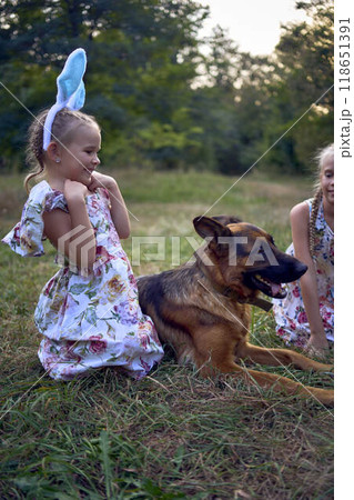 little girls sisters play with german shepherd dog during easter picnic in the garden little girls sisters play with german shepherd dog during easter picnic in the garden 118651391