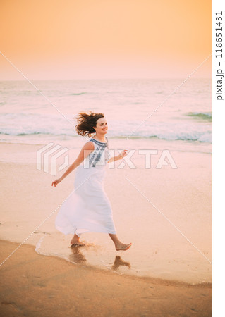 Goa, India. Young Caucasian Woman With Fluttering Hair In Wind In White Dress Walking Along Seashore, Enjoying Life And Smiling In Summer Sunlight Goa, India. Young Caucasian Woman With Fluttering Hair In Wind In White Dress Walking Along Seashore, Enjoying Life And Smiling In Summer Sunlight 118651431