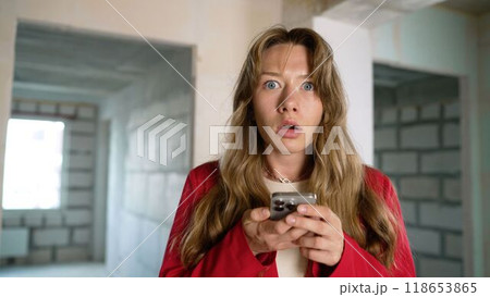 Shocked woman reading bad news on smartphone in unfinished apartment. Shocked woman reading bad news on smartphone in unfinished apartment. 118653865