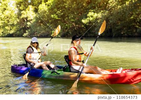 Two young women floating and smiling in a kayak on the river.  118654373