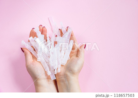 Medical eye drops in plastic pipettes on pink background. Pile of empty plastic ampoules for drops in hands. Plastic vials of saline solution 118657503
