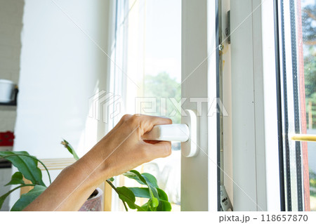 The hand holds the handle of a plastic double-glazed window, closing and opening the window with a rotary mechanism, the position of the handle for ventilation, micro-ventilation The hand holds the handle of a plastic double-glazed window, closing and opening the window with a rotary mechanism, the position of the handle for ventilation, micro-ventilation 118657870