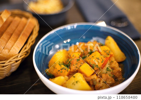 yellow food in a blue plate. vegetable stew with potatoes carrots pepper sprinkled with herbs. High quality photo food on a wooden table. The view of the food is shot at 45 degrees. There is also 118658480
