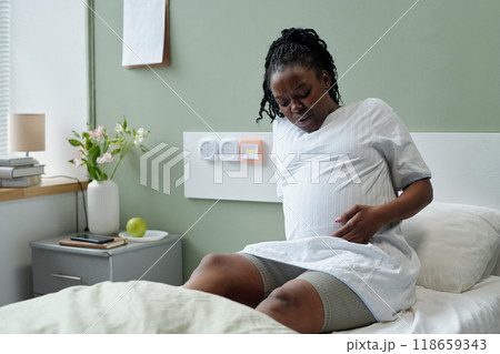 Pregnant Woman Sitting in Hospital Room Holding Belly 118659343