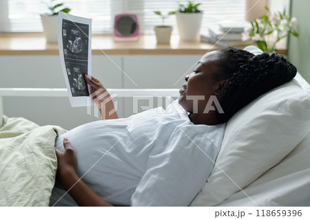Pregnant Woman Examining Ultrasound Photos While Resting 118659396