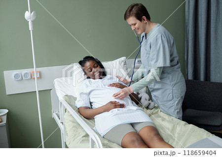 Caring Nurse Checking on Patient in Hospital Bed 118659404