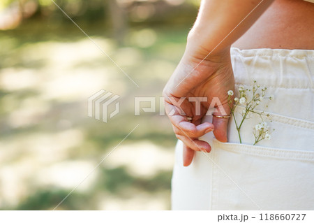 female hand on the back pocket of white pants, with a small spri female hand on the back pocket of white pants, with a small spri 118660727