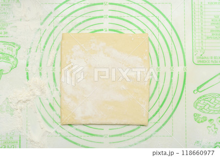 Square dough sheet on green silicone pastry mat with flour dusting. Square dough sheet on green silicone pastry mat with flour dusting. 118660977