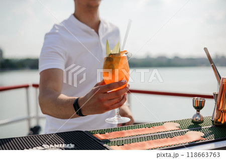Refreshing Summer Cocktail in Hand at Outdoor Bar Overlooking Scenic Water View Refreshing Summer Cocktail in Hand at Outdoor Bar Overlooking Scenic Water View 118663763