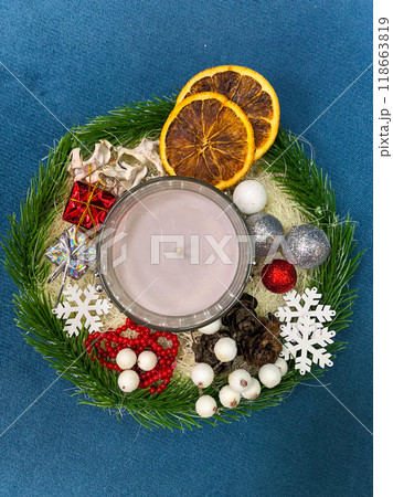A festive Christmas arrangement featuring a lit candle, dried oranges, ornaments, and holiday decorations on a blue background. holiday season and warm inviting atmosphere. Celebration and xmas A festive Christmas arrangement featuring a lit candle, dried oranges, ornaments, and holiday decorations on a blue background. holiday season and warm inviting atmosphere. Celebration and xmas 118663819