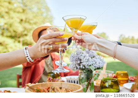 Group of friends raising glasses during celebration at outdoor dining area. Table filled with various dishes and drinks, with everyone enjoying the festive atmosphere 118665520