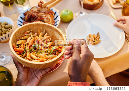 Close-up view of people enjoying pasta salad and other dishes on a beautifully set table during outdoor meal gathering Close-up view of people enjoying pasta salad and other dishes on a beautifully set table during outdoor meal gathering 118665521