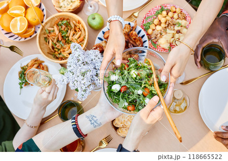Table filled with variety of Mediterranean dishes being served, showing hands with plates and drinks capturing the vibrant communal meal setting, group gathering during daylight 118665522