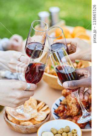 Close-up of hands raising wine glasses during picnic including snacks, olives, and crackers on table. Cheers and camaraderie in outdoor setting with diverse participants Close-up of hands raising wine glasses during picnic including snacks, olives, and crackers on table. Cheers and camaraderie in outdoor setting with diverse participants 118665526