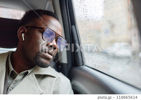 Man wearing glasses and earbuds, sitting in a car on a rainy day, staring out window with a pensive expression, wearing beige jacket Man wearing glasses and earbuds, sitting in a car on a rainy day, staring out window with a pensive expression, wearing beige jacket 118665614