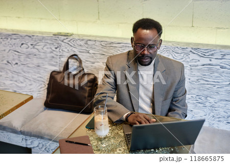 African American man sitting in modern cafe booth, working on laptop with concentration, drink and bag beside him 118665875