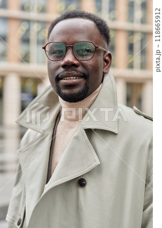 Portrait of smiling African American man wearing glasses and standing outside in urban setting with modern buildings in background on a cloudy day Portrait of smiling African American man wearing glasses and standing outside in urban setting with modern buildings in background on a cloudy day 118665912