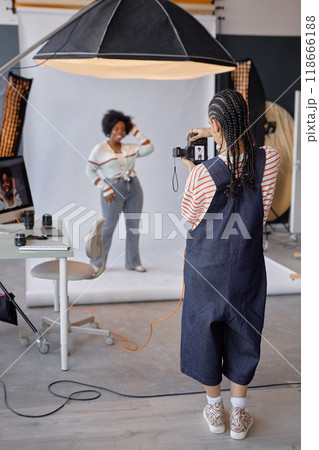 Full length back view of young woman as female photographer taking pictures of model in professional photo studio 118666188