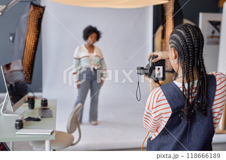 Back view of young African American woman taking pictures of female model on white background in professional photo studio, copy space 118666189