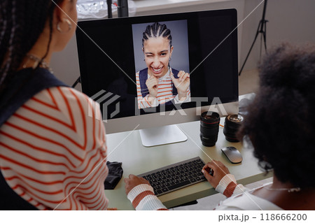 Over shoulder view at two women looking at portrait pictures on computer screen during photo selection in professional photoshoot 118666200