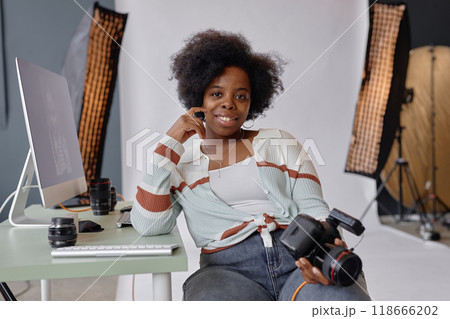 Portrait of smiling African American woman as photographer looking at camera at workplace in photo studio and holding camera, copy space 118666202