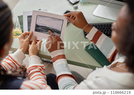High angle closeup of two African American two women collaborating on creative project and holding photo prints with nature landscapes 118666219