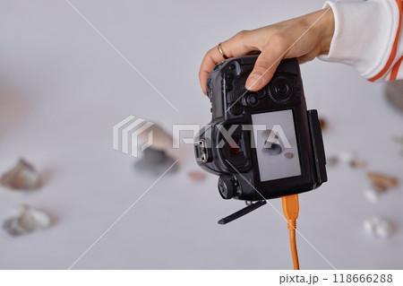 Closeup of female hand holding pro DSLR camera and taking product pictures in minimal studio set copy space 118666288