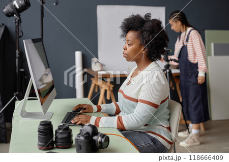 Side view portrait of Black female photographer using computer for edit and retouch in professional photo studio copy space Side view portrait of Black female photographer using computer for edit and retouch in professional photo studio copy space 118666409