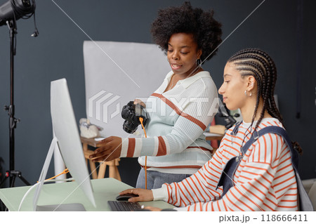 Side view portrait of two African American young women as female photographers collaborating in photo studio and looking at pictures on computer screen 118666411