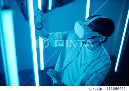 Portrait of man wearing VR headset interacting with blue neon lights and reaching out experiencing digital cyberspace during modern art show 118666432