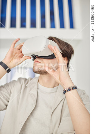 Vertical portrait of man using VR headset in minimal white setting of futuristic smart home or modern art museum 118666469