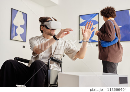 Side view portrait of man with disability using wheelchair and wearing VR tech while interacting with invisible artwork in accessible modern art exhibition copy space 118666494