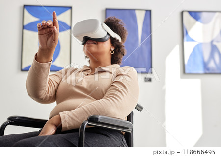Low angle portrait of Black woman with disability wearing VR and pointing with index finger while enjoying mixed reality experience 118666495