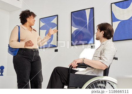 Side view portrait of smiling Black woman talking to man using wheelchair in accessible modern art gallery and discussing abstract paintings Side view portrait of smiling Black woman talking to man using wheelchair in accessible modern art gallery and discussing abstract paintings 118666511