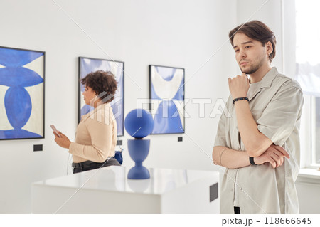 Minimal portrait of young man looking at modern art sculpture while visiting gallery or museum in white and blue tones copy space 118666645