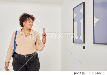 Minimal waist up portrait of smiling Black woman taking pictures of abstract art paintings while visiting modern art gallery exhibition copy space 118666650