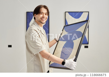 Minimal waist up portrait of smiling young man holding abstract art painting and looking at camera in modern art gallery copy space 118666673