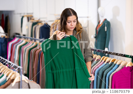 Young woman studying the fabrics of modern green sleeveless cardigan in a clothing store Young woman studying the fabrics of modern green sleeveless cardigan in a clothing store 118670379