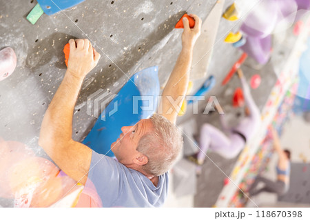 Alpinist practicing indoor rock climbing on artificial boulder without safety belts 118670398