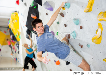 Man showing thumb up while exercising on artificial climbing wall Man showing thumb up while exercising on artificial climbing wall 118670620