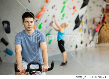 Young man riding exercise bike in climbing gym 118670671