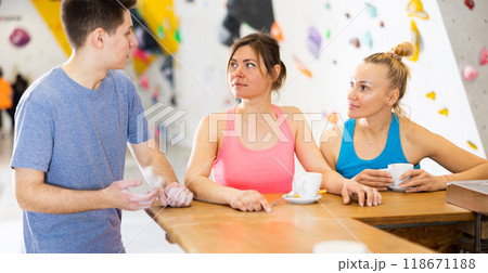 Two sports women and a guy communicate after training on a climbing wall at a table in cafe 118671188
