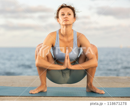 Woman practicing yoga on sea beach, stretching in an asymmetrical seated asana Parivritta Janu Sirsasana 118671278