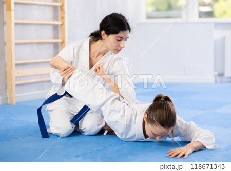 Sportive woman holds her opponent by force while sitting on mats during judo classes 118671343