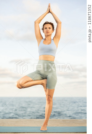 Athletic female yoga practitioner performing Garudasana on beach 118671352