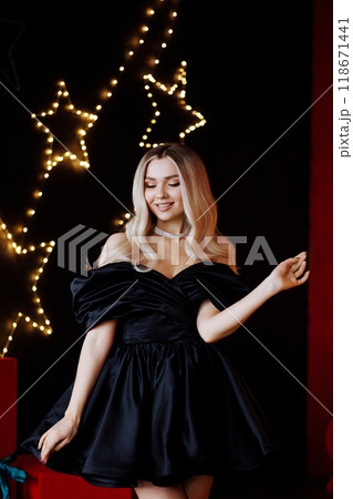 Blonde woman in black dress posing for photo in front of Christmas tree Blonde woman in black dress posing for photo in front of Christmas tree 118671441