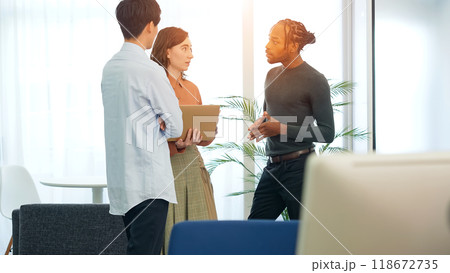 オフィスでノートパソコンを見ながら会話する多国籍の人々 118672735