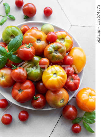 Fresh assorted tomatoes arranged on a white plate with green basil leaves Fresh assorted tomatoes arranged on a white plate with green basil leaves 118674575