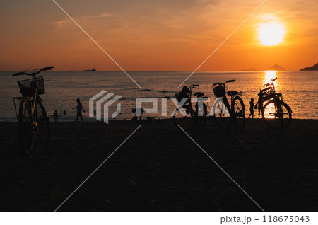 Silhouettes of people and bicycles on beach by the sea in the morning at sunrise in summer on vacation 118675043