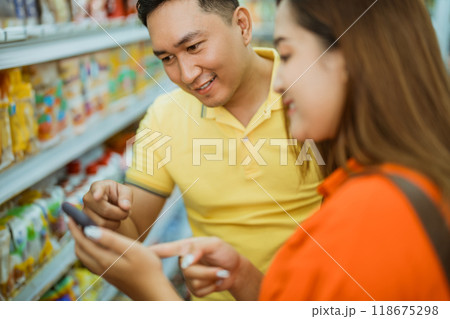 Asian man pointing mobile phone shown by young woman in supermarket 118675298